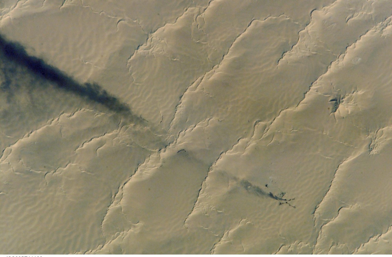 Smoke from a well-head flare drifting across the linear dunes of the Calanscio Sand Sea, seen from orbit